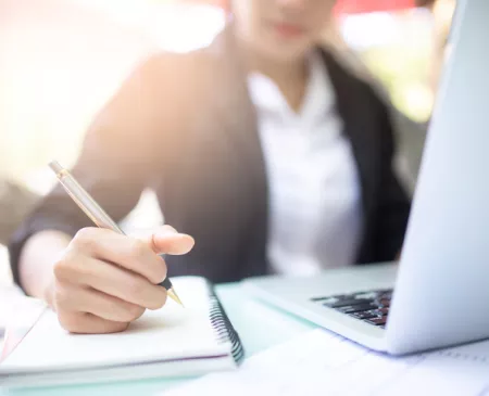 woman writing on notepad with laptop