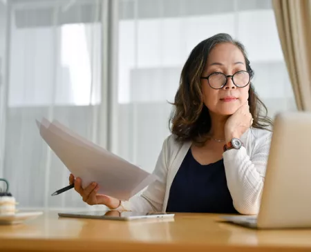 older woman reviewing paperwork and reading laptop